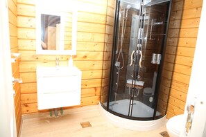 A wooden cabin bathroom with a glass-enclosed shower, a white sink, and a mirror above the sink.