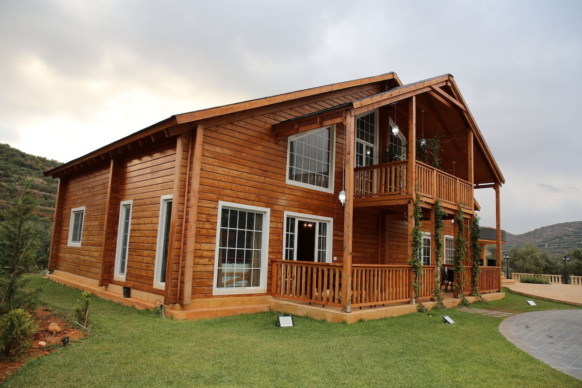 A wooden cabin with a balcony, large windows, and a grassy yard.