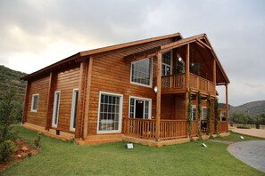 A wooden cabin with a balcony, large windows, and a grassy yard.
