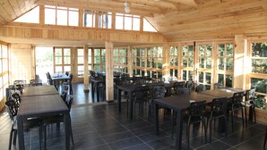 Een ruime eethoek binnen met hoge plafonds en grote ramen, met meerdere tafels en stoelen.