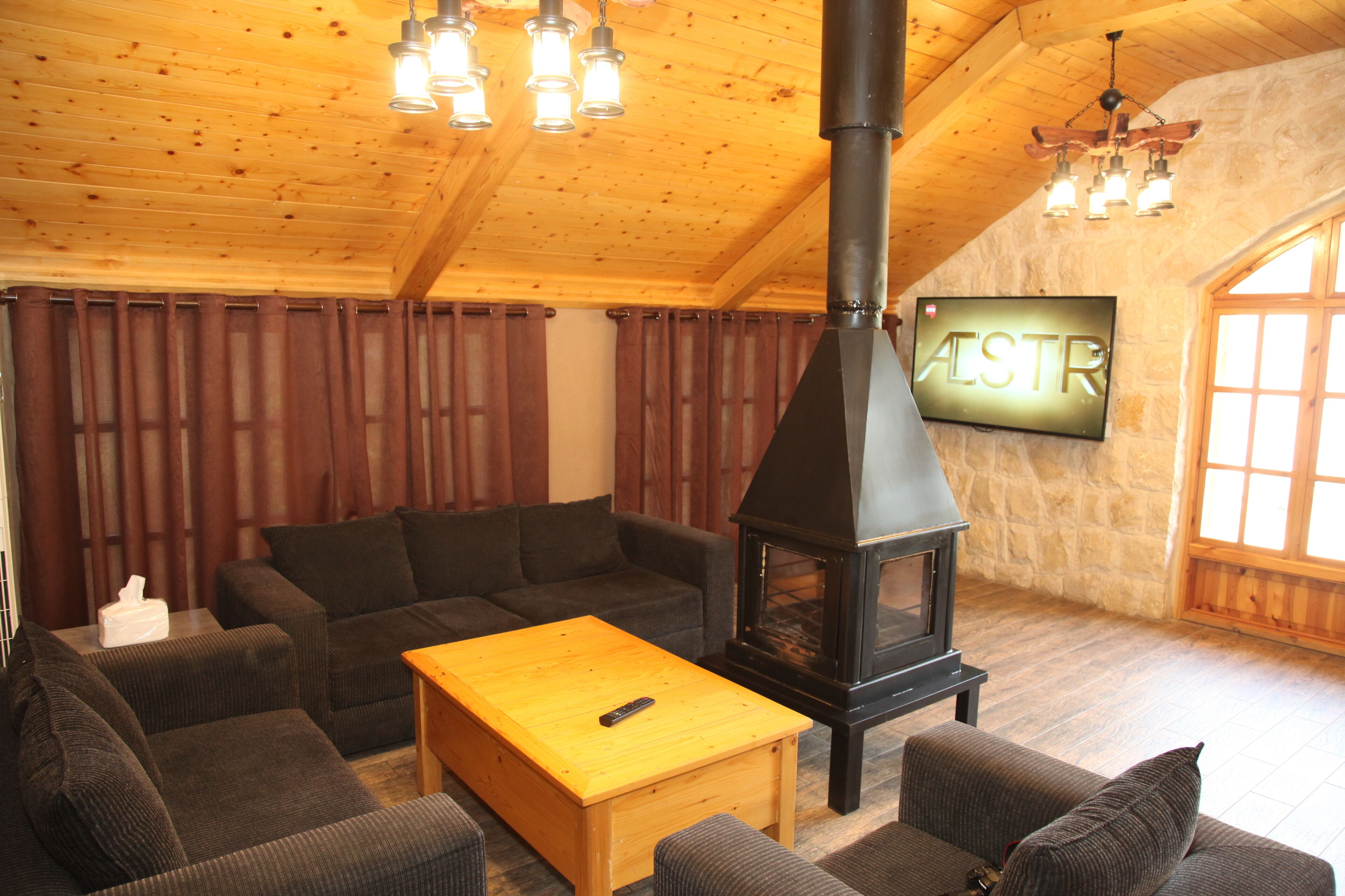 A cozy living room with a fireplace, wooden ceiling, and a television mounted on the wall.