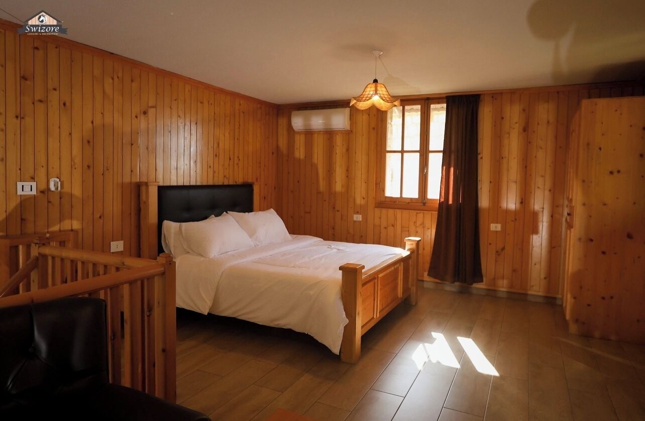A wooden-paneled room with a bed, a window, and a staircase.