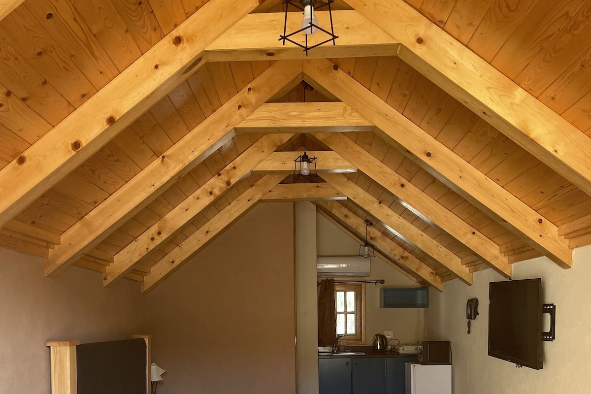 A cozy attic bedroom with a bed, a sofa, a small table, and a kitchen area in the background.