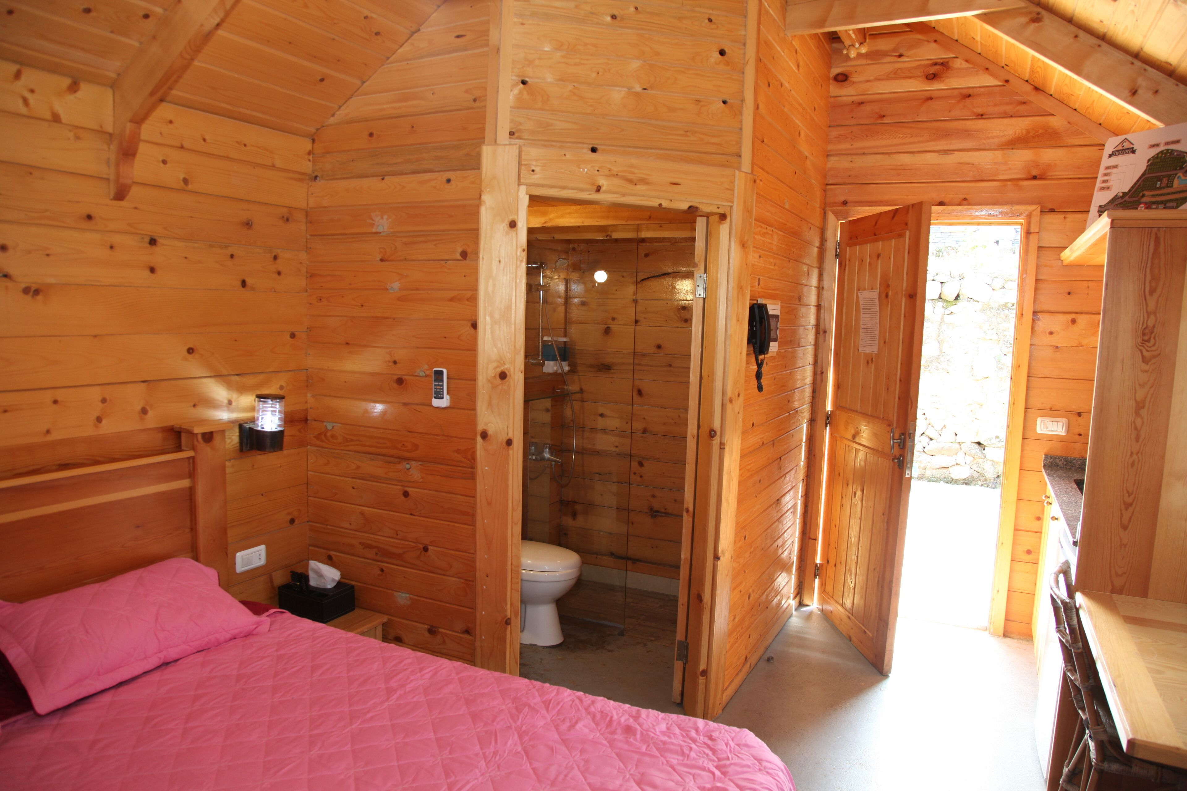 A wooden cabin with a bed, a bathroom, and a small kitchenette.