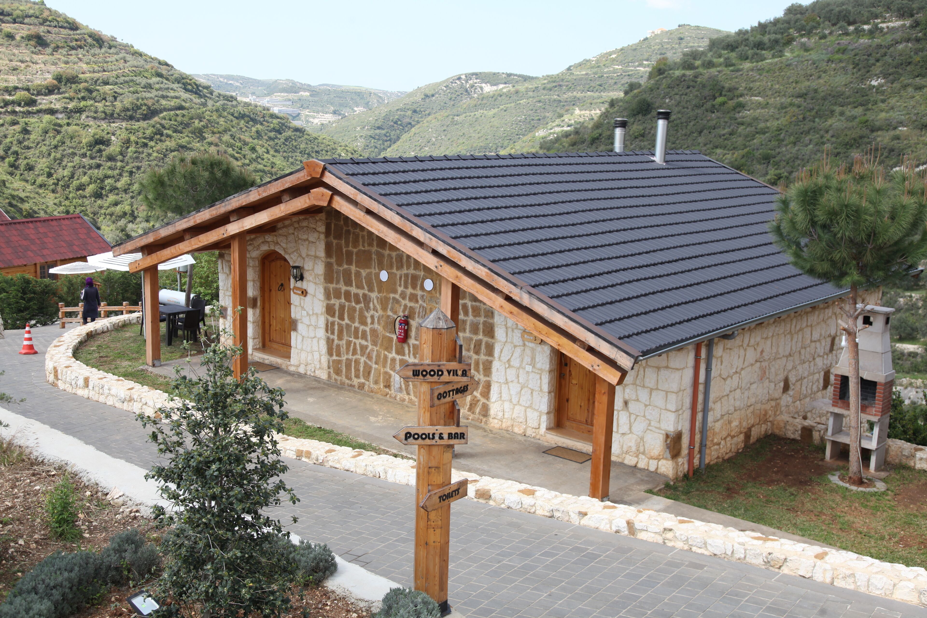 A stone building with a sloped roof, wooden beams, and a signpost indicating directions to 'Wood Yard & Bar' and 'Pool & Bar'.