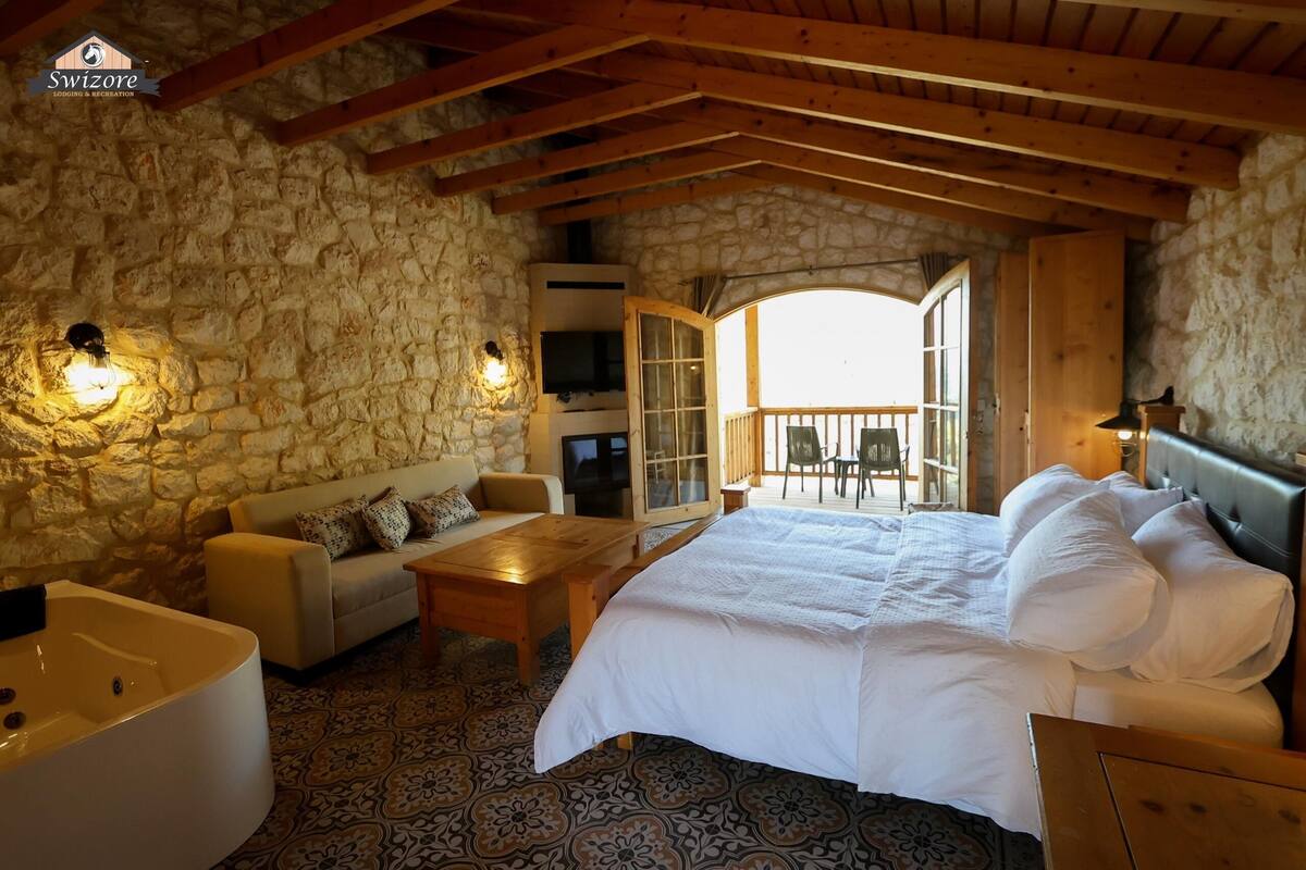 A cozy room with a stone wall, a bed, a sofa, a table, and a TV.