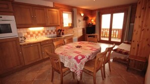 Une cuisine avec des meubles en bois, un sol carrelé, une table à manger avec des chaises et un balcon doté d’une balustrade en bois.