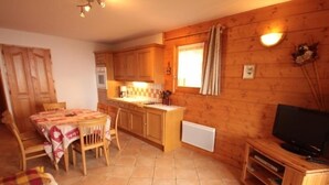 Une pièce confortable, aménagée comme un chalet, avec un intérieur en bois, un coin repas comprenant une table et des chaises, et un téléviseur posé sur un meuble en bois.