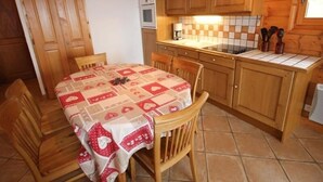 Une cuisine avec des meubles de rangement en bois, un dosseret carrelé et une table recouverte d’une nappe à motifs en forme de cœur.