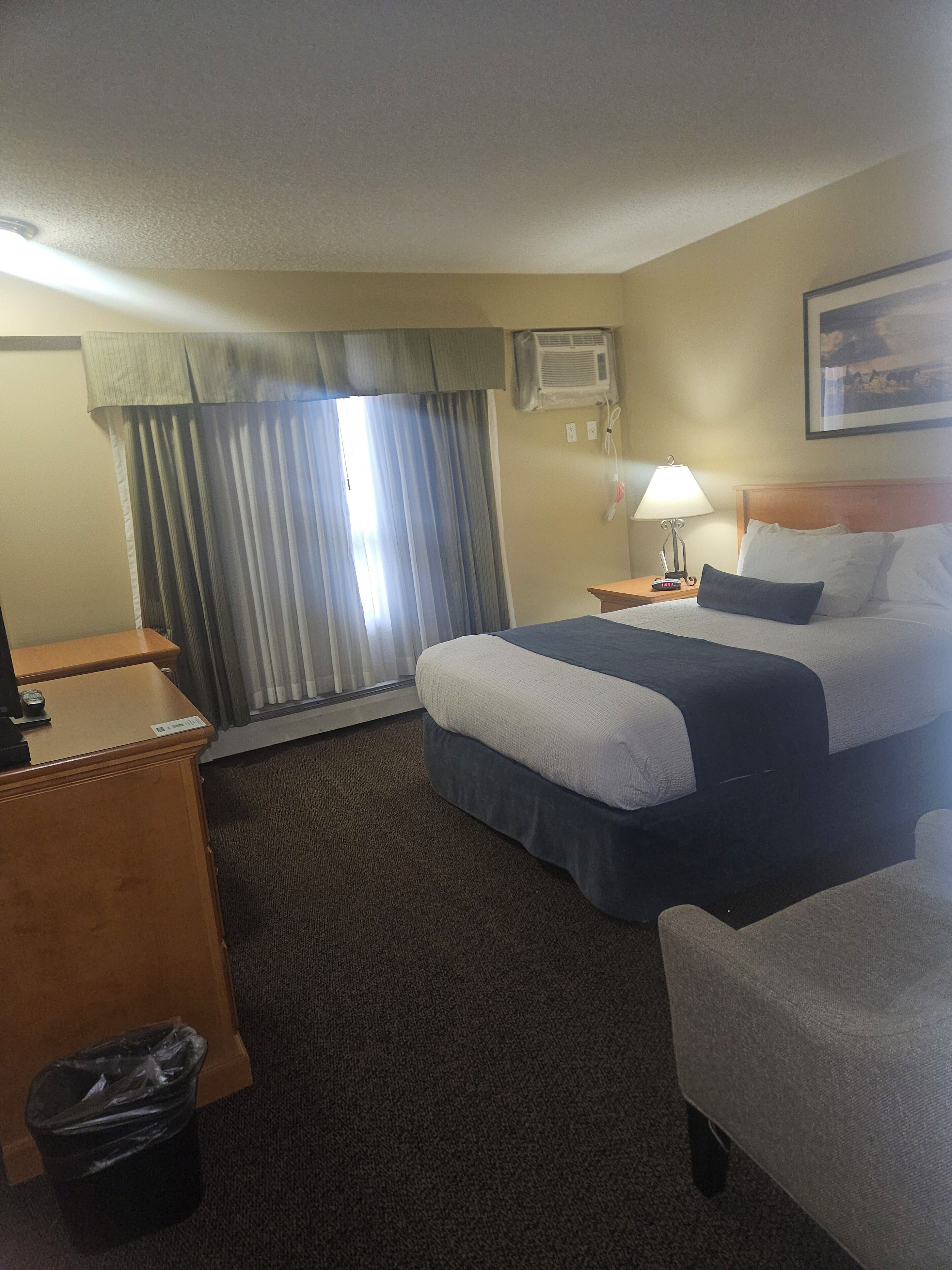 Habitación de hotel con cama, mesita de noche, lámpara y un cubo de basura.