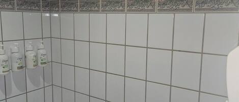 A bathroom with white tiles, a shower, and a toilet.