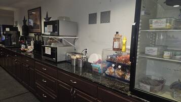 Een kitchenette met een magnetron, koffieapparaat en diverse etenswaren op het aanrecht.