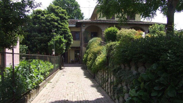 A paved pathway leading to a building with a tiled roof and arched entrance.