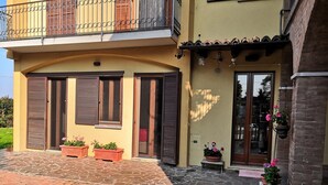 A two-story house with a stone-paved entrance, wooden shutters, and potted plants.