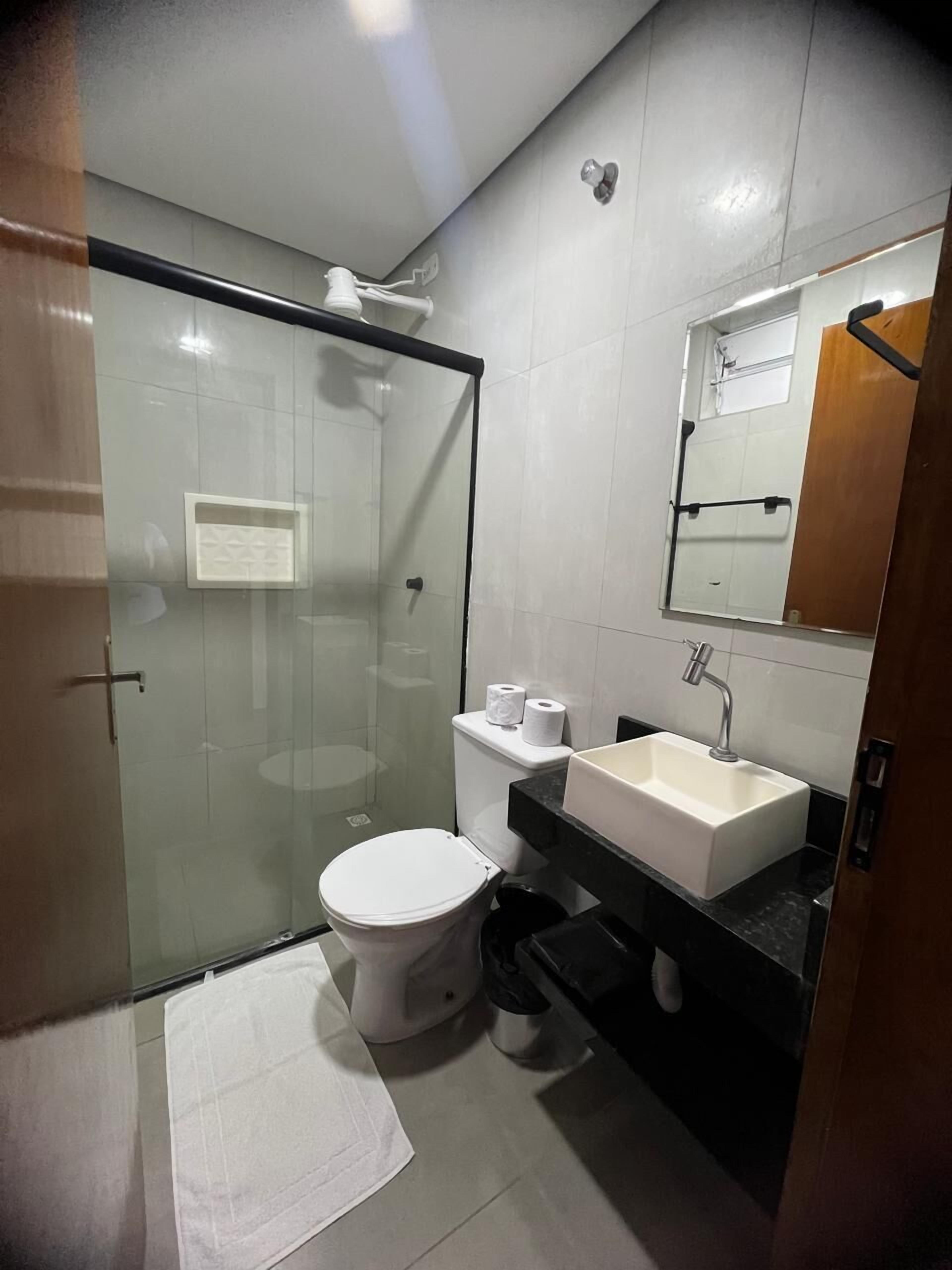 Un baño moderno con ducha de vidrio, inodoro blanco, lavamanos con espejo y una toalla en el suelo.
