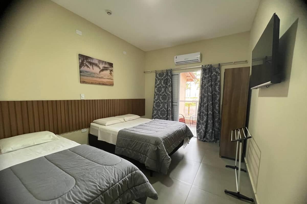 Hotellihuone, jossa on kaksi sänkyä, taulutelevisio, ilmastointilaite ja taulu seinällä.