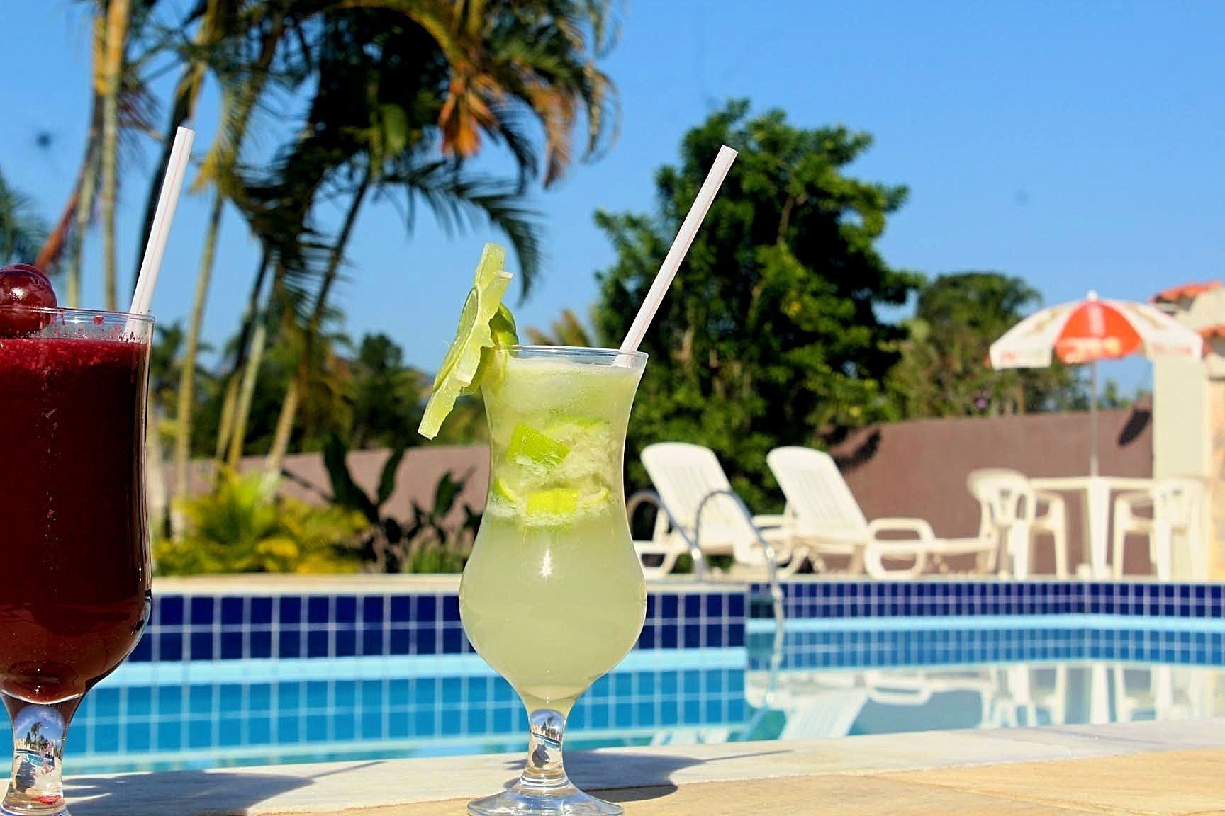 Two cocktails by a poolside with lounge chairs and umbrellas in the background.