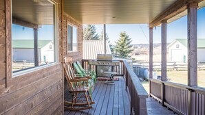 Une terrasse en bois avec des fauteuils à bascule et un barbecue, offrant une vue sur un paysage rural.