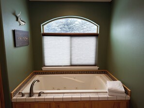Une salle de bain avec une baignoire sur pieds, une fenêtre avec des stores et un poisson décoratif accroché au mur.