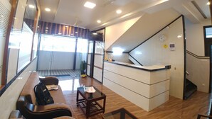 A modern hotel lobby with a reception desk, seating area, and a staircase. - Hotel Jagadguru (Mawal)