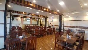 A spacious restaurant with wooden tables and chairs, ceiling fans, and recessed lighting. - Hotel Jagadguru (Mawal)