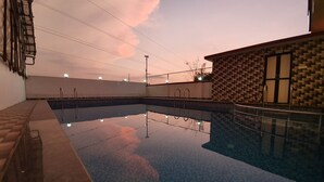 A swimming pool with clear water, surrounded by a tiled wall and a brick wall with a window. - Hotel Jagadguru (Mawal)