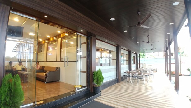 A modern hotel lobby with glass walls, a seating area, and a dining section. - Hotel Jagadguru (Mawal)