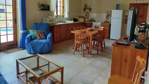 A cozy kitchen with wooden cabinets, a dining table, and a blue armchair. - Dun Nastas Farmhouse (Sannat)