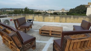 A rooftop terrace with wooden furniture, a table, and a chair. - Dun Nastas Farmhouse (Sannat)