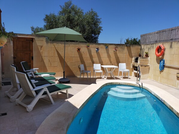 A pool area with lounge chairs, a table, and an umbrella.