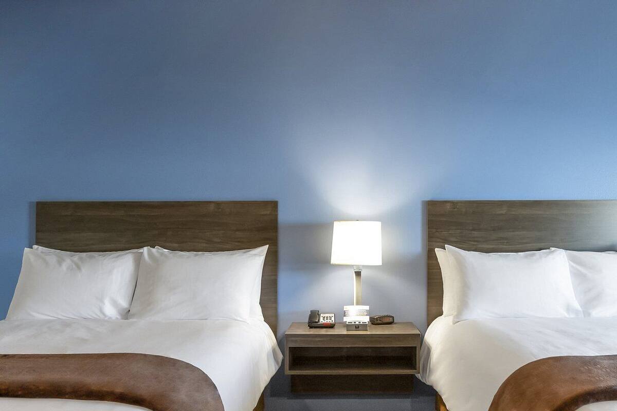 A hotel room with two beds, a nightstand with a lamp, and a small table.