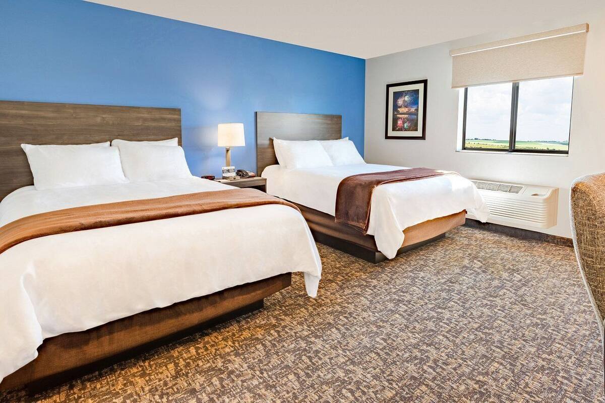 A hotel room with two beds, a window with a view, a heater, and a chair.