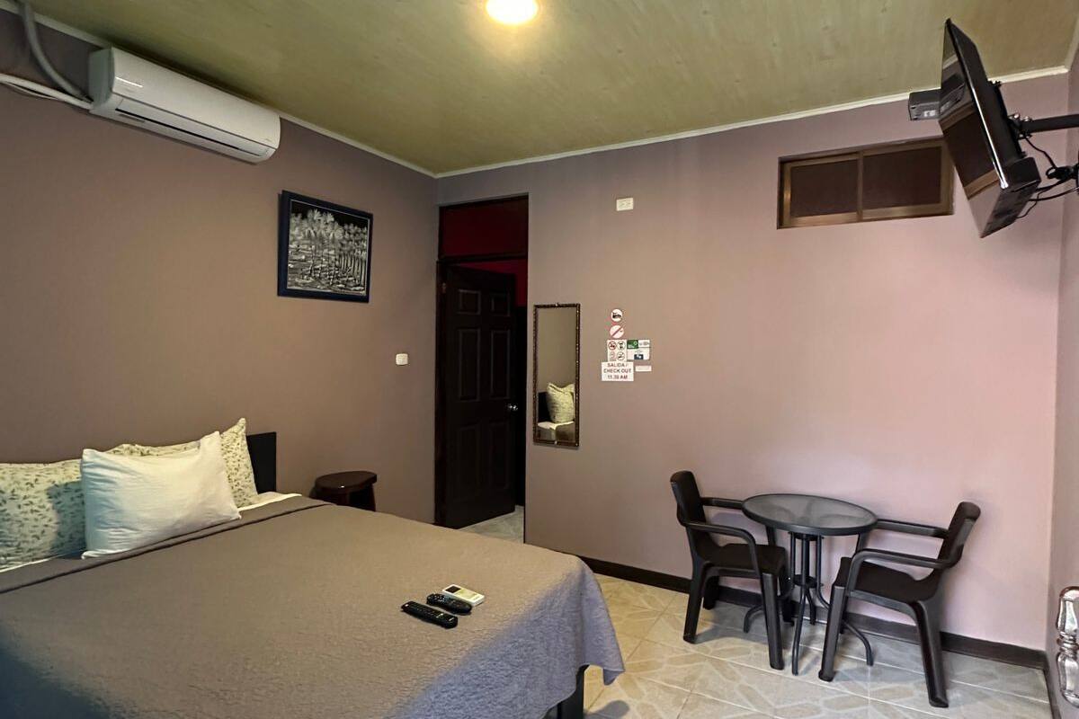 A hotel room with a bed, a desk, a chair, a TV, and an air conditioning unit.