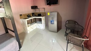 A compact kitchen with a built-in stove, a refrigerator, and a small dining area with a chair and table. - Cabinas Hukats Secret Jungle (Cahuita)