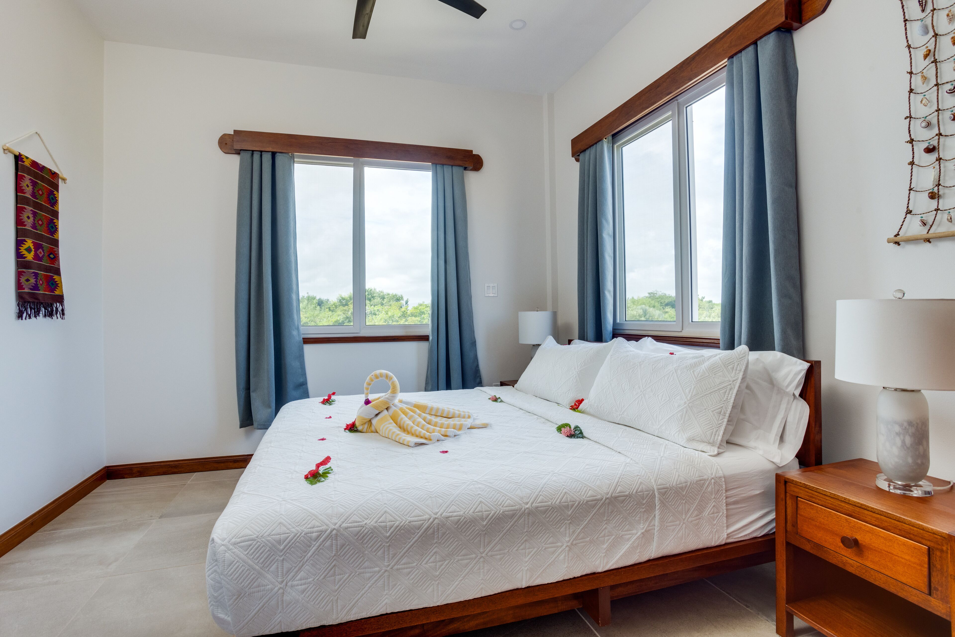 A neatly made bed with a white duvet, a wooden nightstand with a lamp, and a wall-mounted decorative piece.