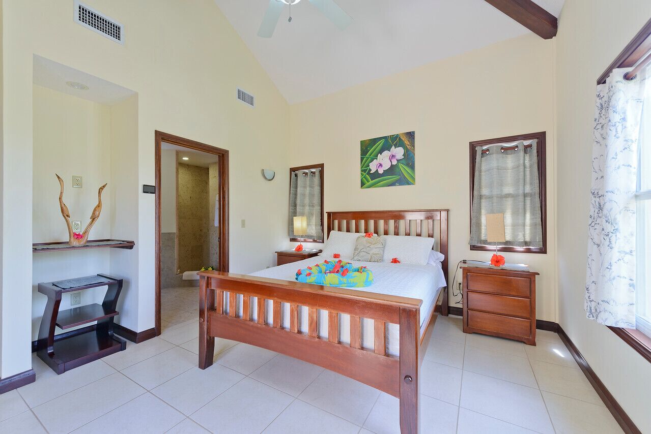 Un dormitorio con una cama de madera, mesitas de noche, un tocador, un espejo y una ventana con cortinas.