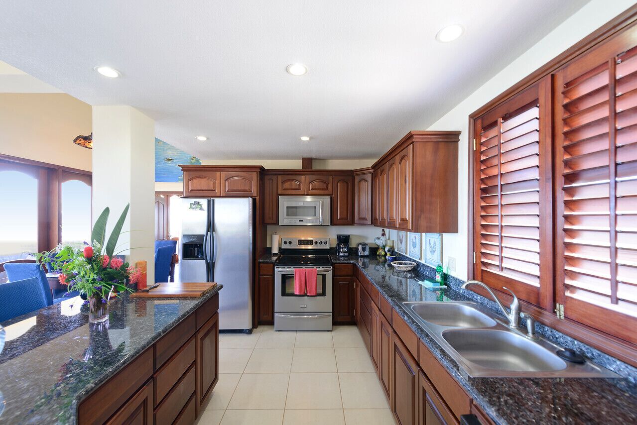 A kitchen with wooden cabinets, stainless steel appliances, granite countertops, and a window with blinds.