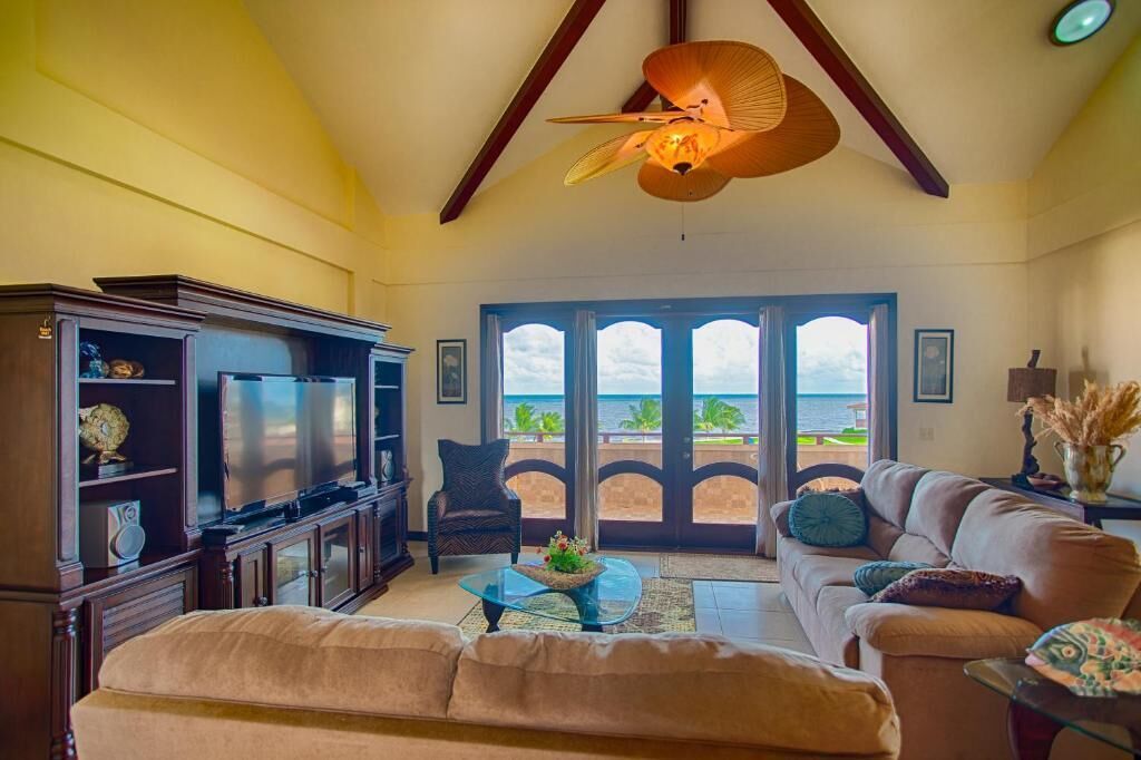 Salón con televisor, sofá y mesa de centro, con vista a un balcón y al océano.