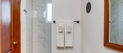 A bathroom with a wooden door, a shower with marble tiles, a toilet, and a sink with a granite countertop.