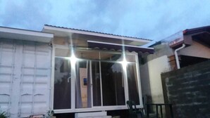 A house with a garage door, a large window with curtains, and a small porch area. - villa with a private garage ,build out of shipping container,fll two rooms and two bathrooms ,dining kitchen ,plenty outdoor space for barbecue (San Miguel)