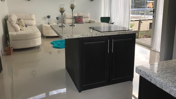 A modern kitchen with a central island, a dining area with a white sofa and a green chair, and a view of a balcony with a railing. - villa with a private garage ,build out of shipping container,fll two rooms and two bathrooms ,dining kitchen ,plenty outdoor space for barbecue (San Miguel)