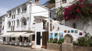 A white building with a balcony, a black door, and a small garden with potted plants and flowers. - La Mariquilla, rural housing in Jubrique, Valle del Genal, natural paradise ... (Jubrique)