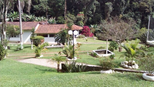 Un jardí exuberant amb un edifici que té teulades ceràmiques, envoltat de plantes i arbres diversos.