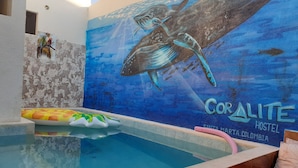 A swimming pool with a mural of a shark and coral, a stone wall, and a colorful inflatable ring. - Coralite Hostel (Santa Marta)