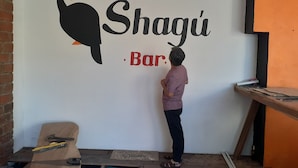 A person painting a wall with the words "Shagui Bar" and a toucan graphic. - Coralite Hostel (Santa Marta)