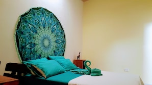 A bed with a green headboard, a wooden nightstand with a giraffe figurine, and a green towel. - Coralite Hostel (Santa Marta)