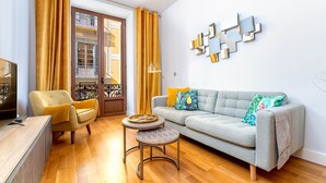 A living room with a grey sofa, yellow armchairs, a small round table, and a TV on a wooden cabinet.