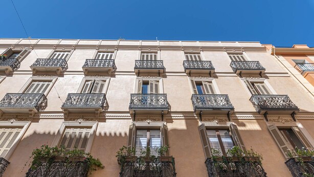 A multi-story building with balconies, windows with shutters, and decorative iron railings.