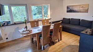 A modern living room with a dining area, large windows, a sofa, and a painting on the wall. - Large cozy apartment "Ziegenpeter" (DG = 2nd floor) - Kolvenbacher Ziegenhof 95sqm (Hohn)