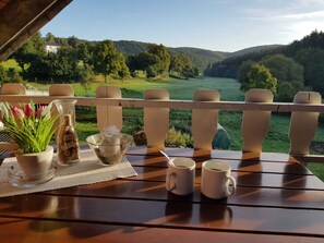 Eine Holzdielen-Terrasse mit einem Tisch für zwei Personen, mit Blick auf eine malerische Landschaft mit Hügeln und Bäumen.